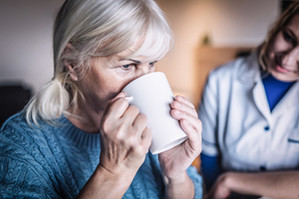 Foto: Eine Dame trinkt Kaffee in Gesellschaft einer Pflegekraft.
